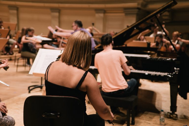 Musikere øver med orkester og flygel på scenen i en konsertsal