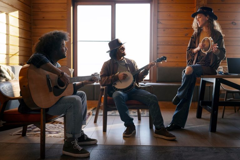 Tre musikere spiller gitar, banjo og tamburin i et lunt rom med trevegger